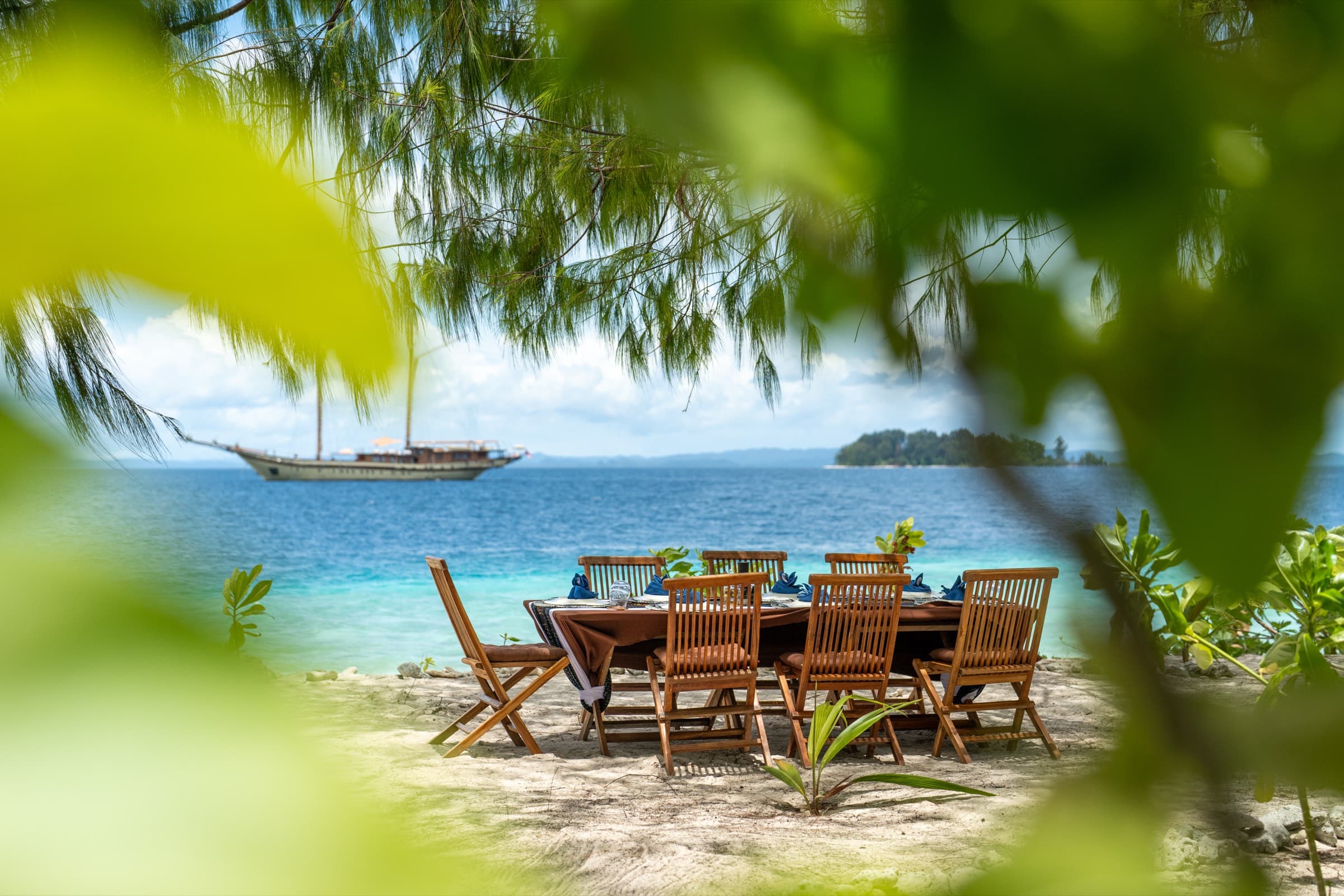 A table laid for eight on a Raja Ampat beach, schooner at anchor offshore